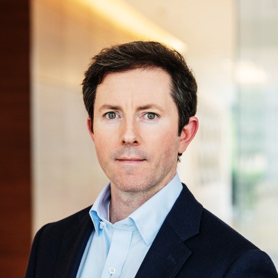 Nathan Frost, Dominion Energy. A man with short dark hair wearing a navy blazer and light blue collared shirt stands in a brightly lit modern office hallway, looking directly at the camera with a neutral expression.