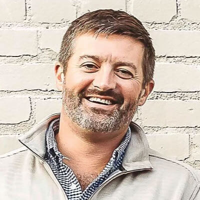 Cory Gordon, Duke Energy. A man with short dark hair and a beard, wearing a suit and tie, smiling at the camera in an outdoor setting with trees in the background.