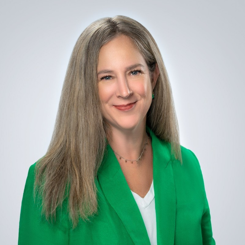 Kari Binley, Tierra Resource Consultants. A woman with long, straight, light brown hair wearing a bright green blazer over a white top, smiling warmly against a plain light gray background.