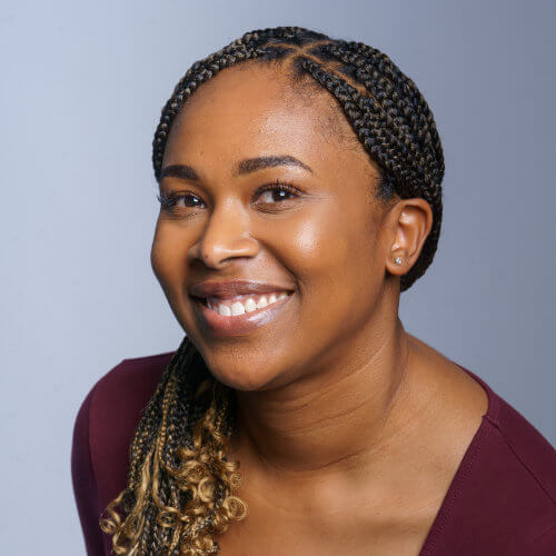 Smiling woman with braided hair, wearing a maroon top, against a plain light gray background.