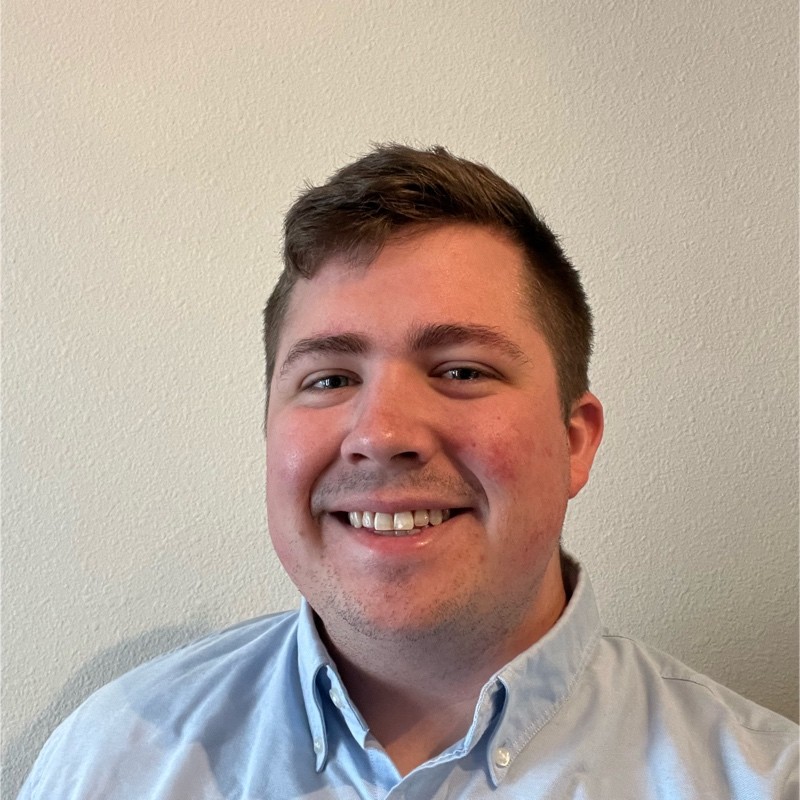 William Robichaux, Parsons. A smiling young man with short brown hair wearing a light blue button-up shirt stands in front of a plain, light-colored wall.
