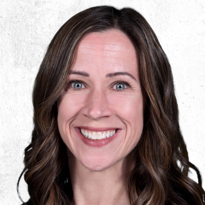 Smiling woman with wavy brown hair, blue eyes, and light skin, in front of a white textured background.