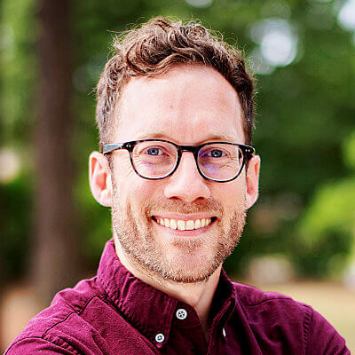 Brian Doherty, Rappahannock Electric Coop. Smiling man with glasses and short curly hair, wearing a maroon shirt, standing outdoors with blurred greenery in the background.