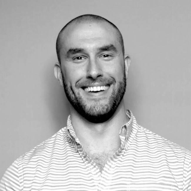 Cameron Seher, Pacific Gas & Electric. Smiling man with a shaved head and beard, wearing a light striped button-up shirt, against a plain background.