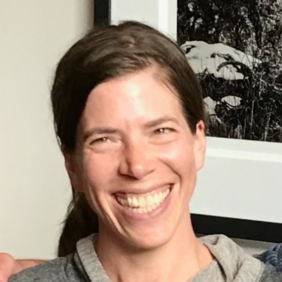 Emma Johnson, Puget Sound Energy. A person with long brown hair smiles broadly, wearing a gray top, standing indoors near a black and white photo.