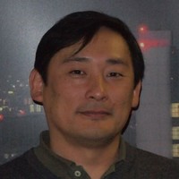 Man with short dark hair and a slight smile, standing in front of a cityscape background at night.
