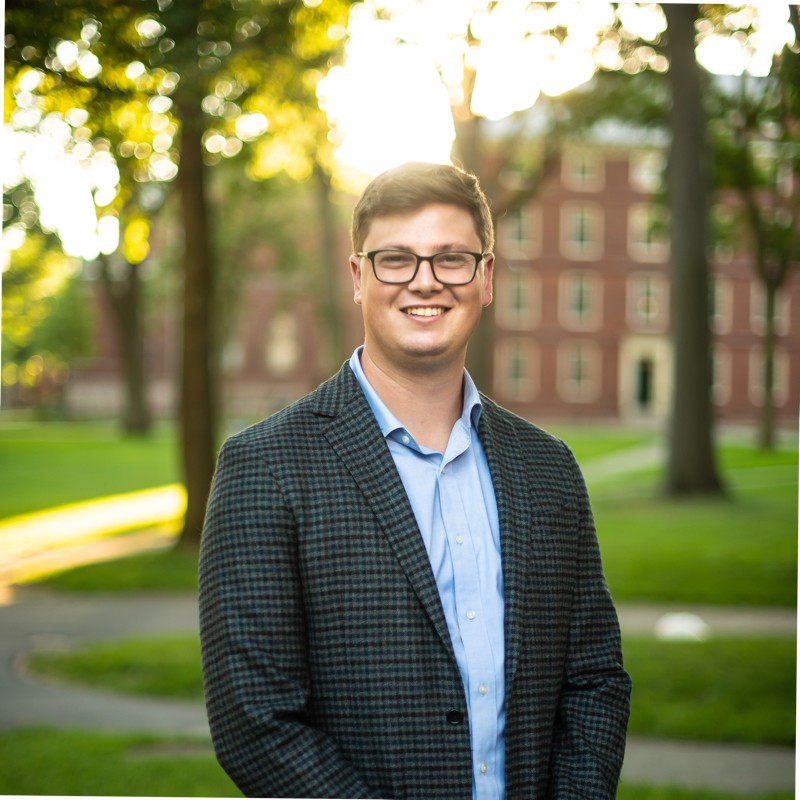 Kipling Haviland-Hack, EnergyHub. A man in glasses and a blazer smiles outside on a campus with trees and a brick building in the background.