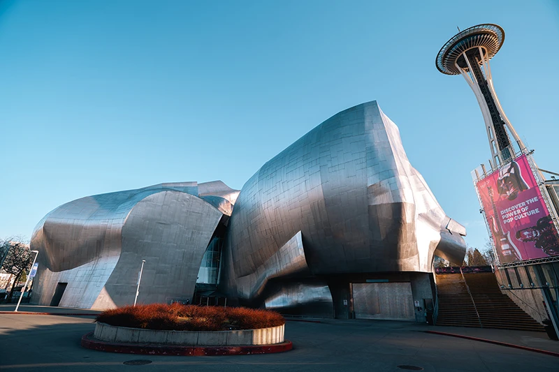 Curved silver building next to the Space Needle under a clear blue sky in Seattle.