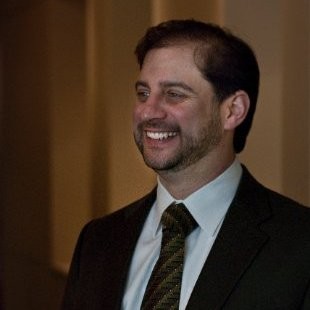 Philip Popoff, Popoff Energy Strategy Consulting. Smiling man in a dark suit, white shirt, and striped tie stands indoors against a softly lit background.