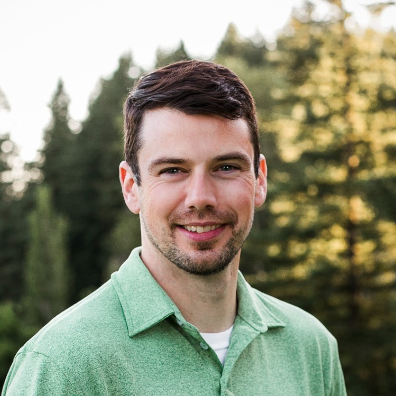 Rick Hodges, Portland General Electric. Smiling man with short dark hair in a green shirt standing outdoors in front of blurred trees.