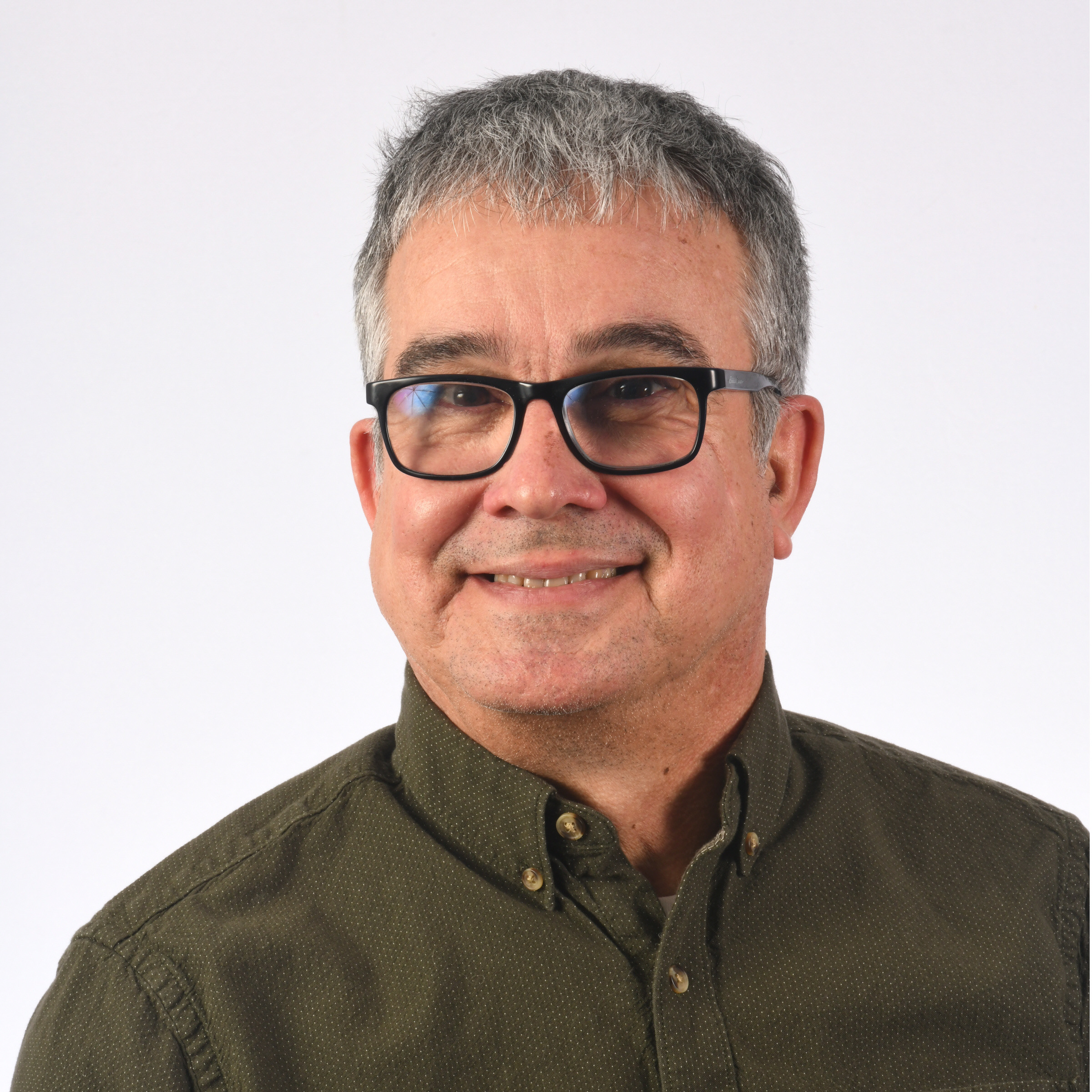 Smiling middle-aged man with gray hair, glasses, and an olive green button-up shirt against a plain white background.